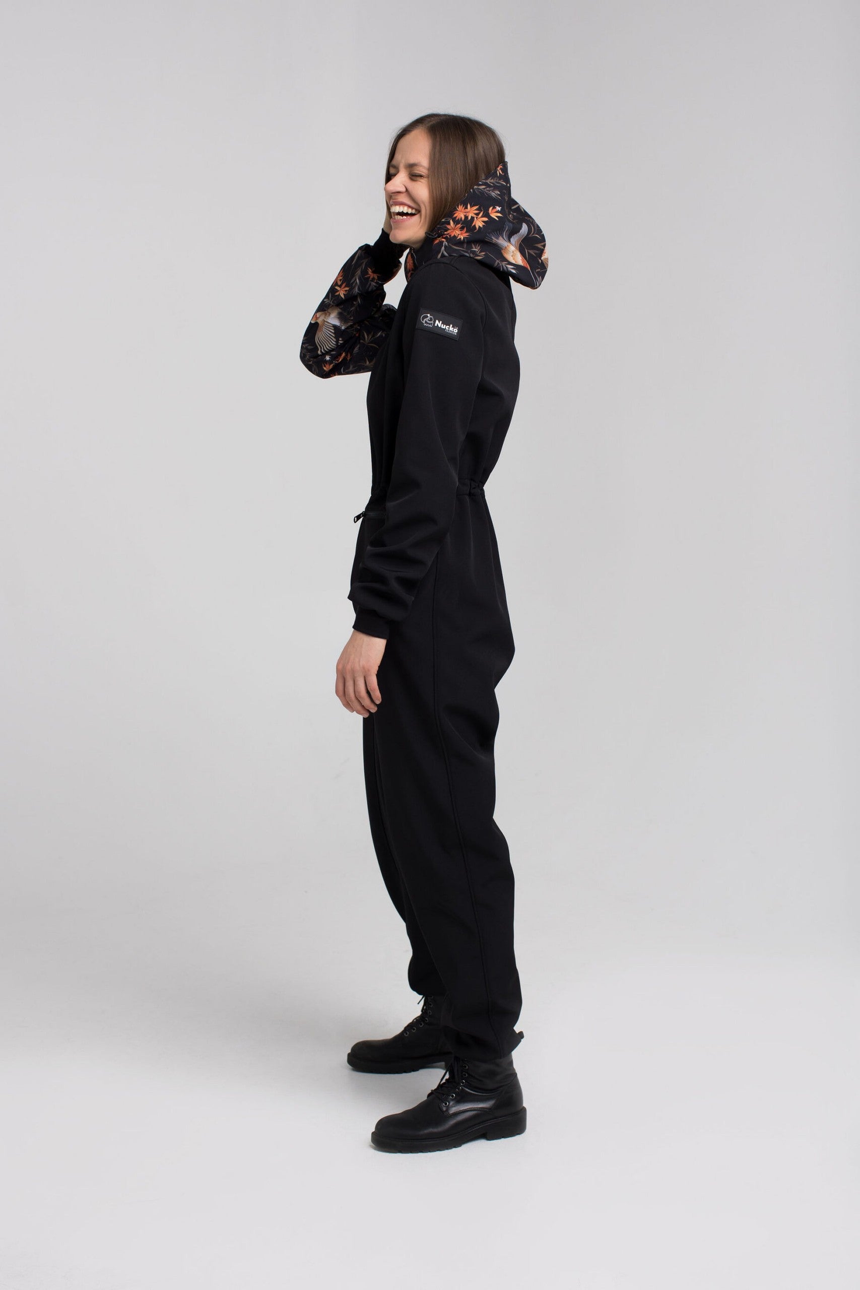 NUCKÖ EMMA softshell kombinezons – sānskats ar regulējamu jostu un kapuci.